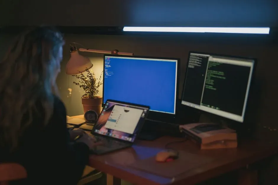 A person sitting at a desk, surrounded by multiple computer screens displaying various analytics dashboards, code, and design software, illustrating the diverse tools and technical skills required in growth marketing. - growth marketing